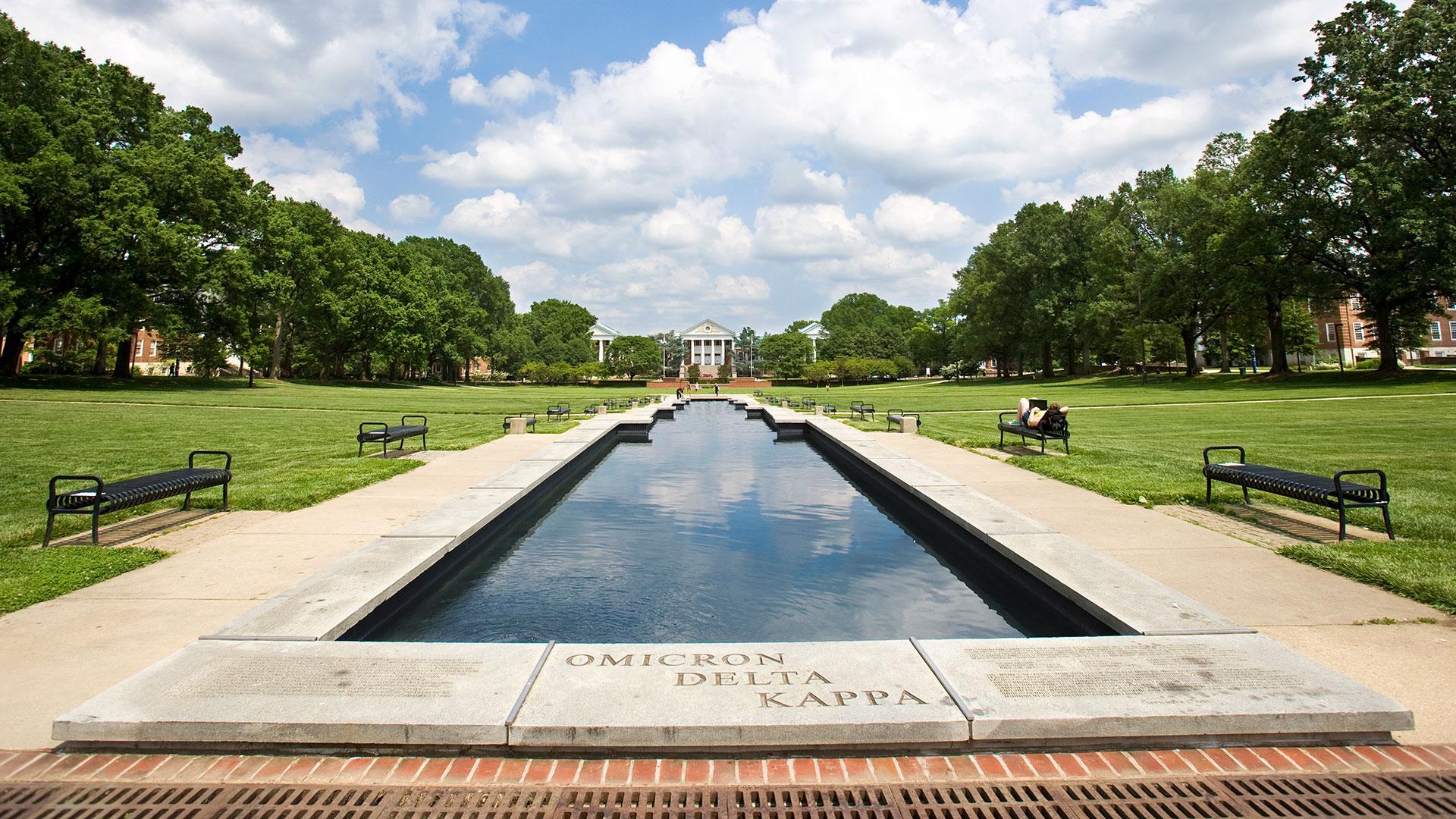 View of ODK Fountain on the Mall, looking towards Main Administration Building. Blue sky, clouds, green grass/trees.