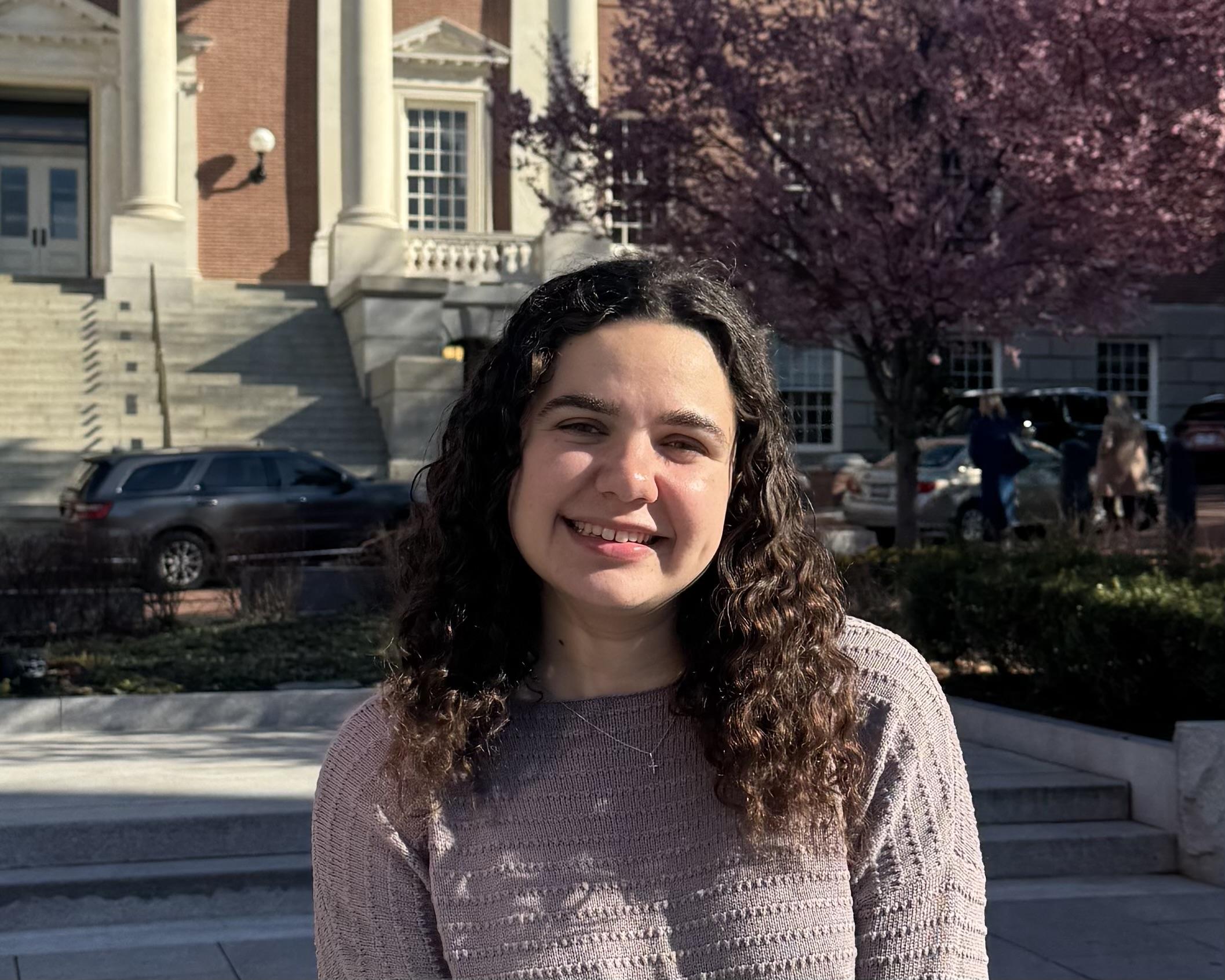 Taryn in front of brown building with pink tree