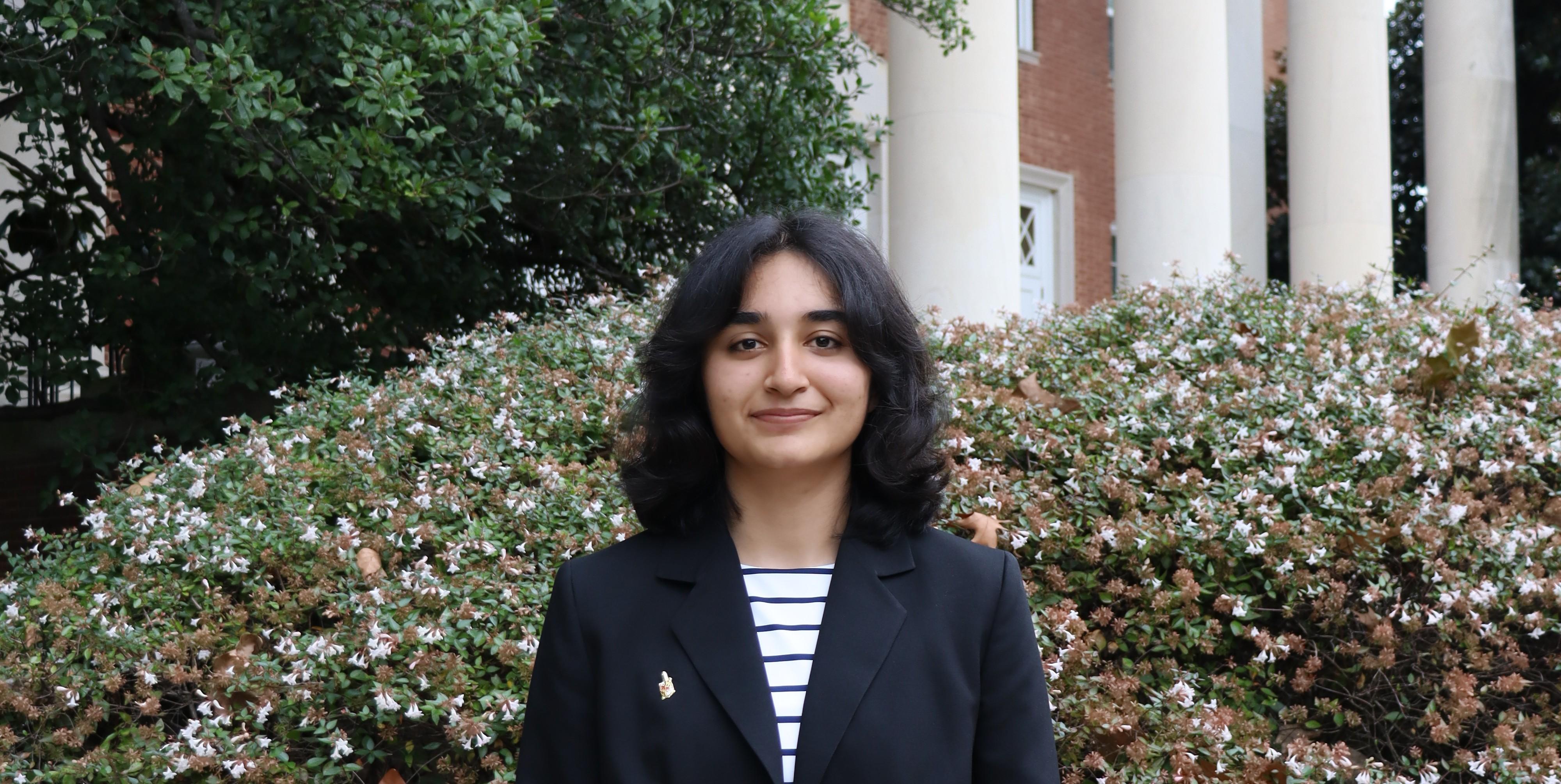 Priya in front of green bush and white columns